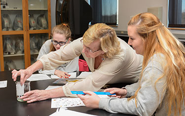 A biology instructor shows students how to test a substance in a beaker.