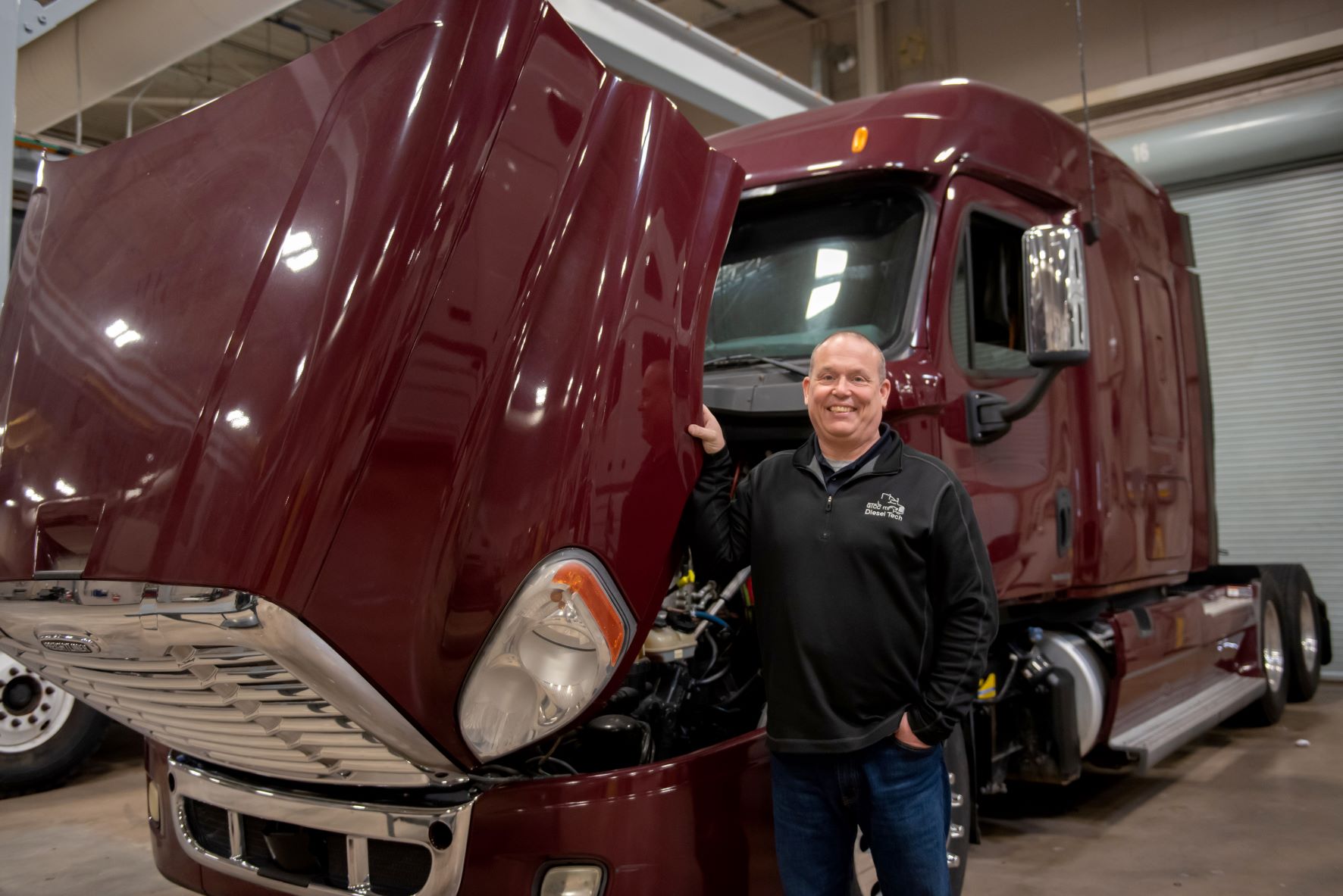 Jonathan Skeen poses for a portrait in front of a truck with its hood up.